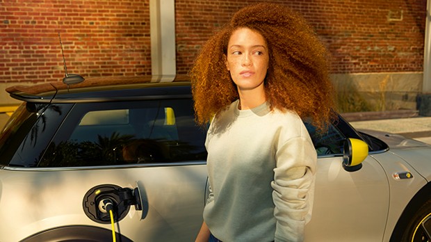 Eine Frau mit braunen Locken steht vor einem MINI Cooper E